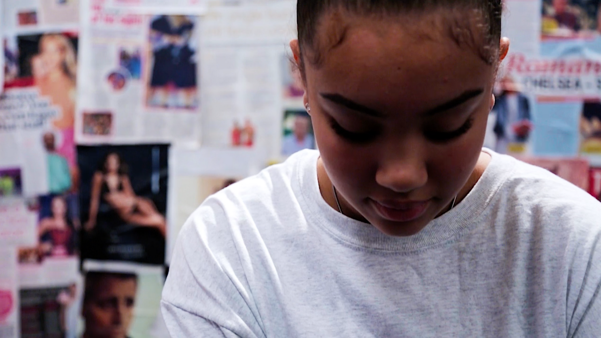 Young girl looking down with a background of magazine pages stuck to a wall