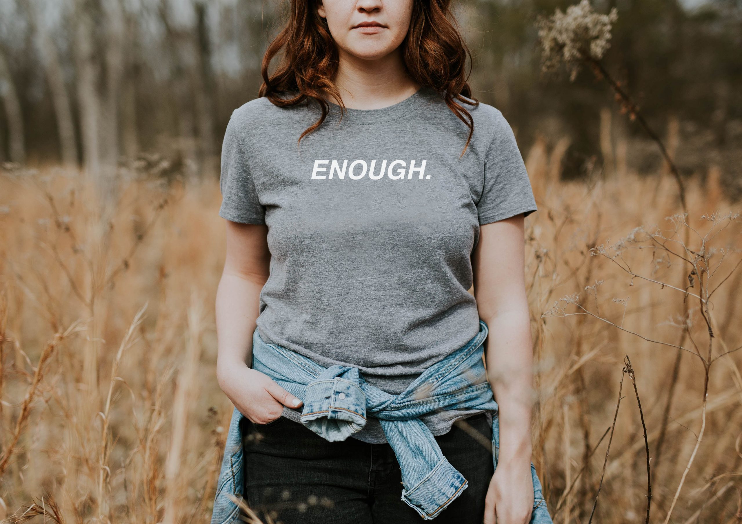 Woman stood in a field wearing grey t-shirt with the word 'enough' printed on