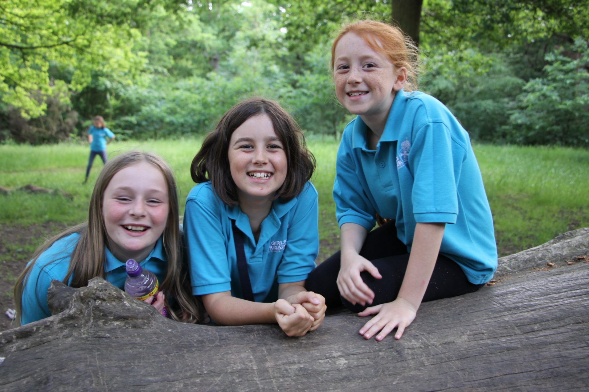 Three girls sitting in a wooded area smiling at the camera