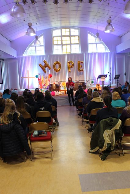 Girls' Brigade volunteers sat listening to speaker with balloons spelling hope in the background