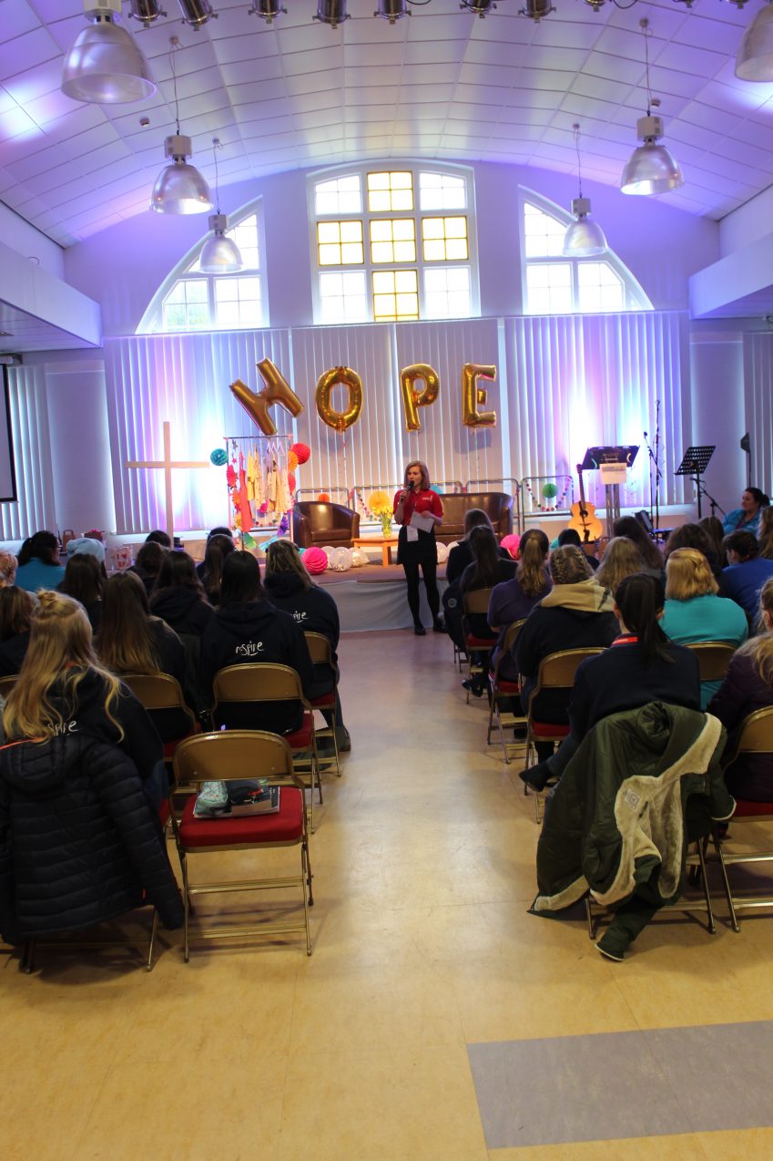 Girls' Brigade volunteers sat listening to speaker with balloons spelling hope in the background