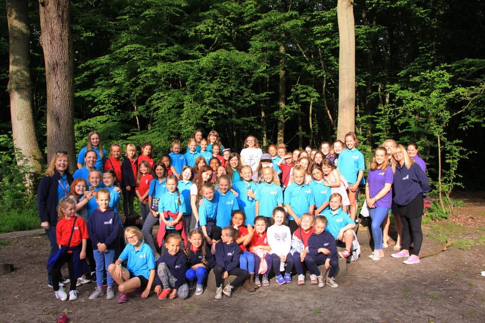 A large group of Girls' Brigade volunteers, girls and young people gathered in front of trees