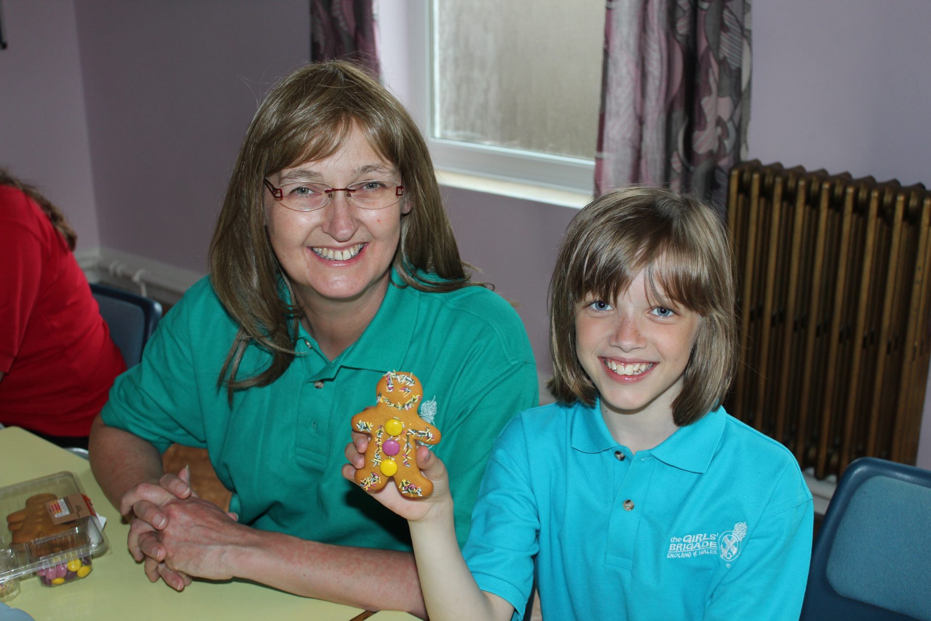 n:gage girls holding up decorated gingerbread man with Girls' Brigade volunteer