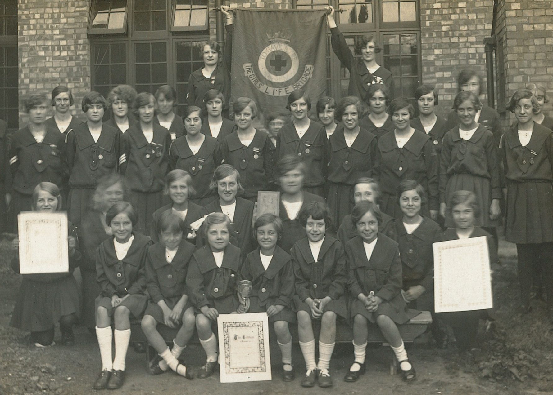 Girls' Life Brigade company sat in rows outside with GLB banner and certificates - black and white photo