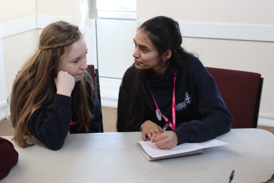 Two Girls' Brigade young leaders chatting and making notes sat at a table