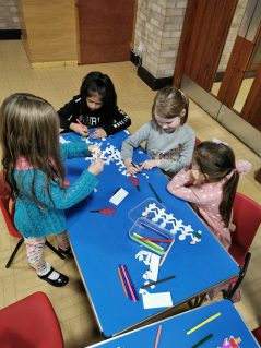 n:vestigate girls sat at table at Bromsgrove making paper chain people