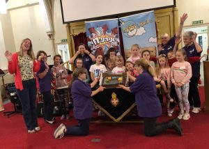 girls and volunteers gathered at front of church, with cake, display table and banners for their grand opening