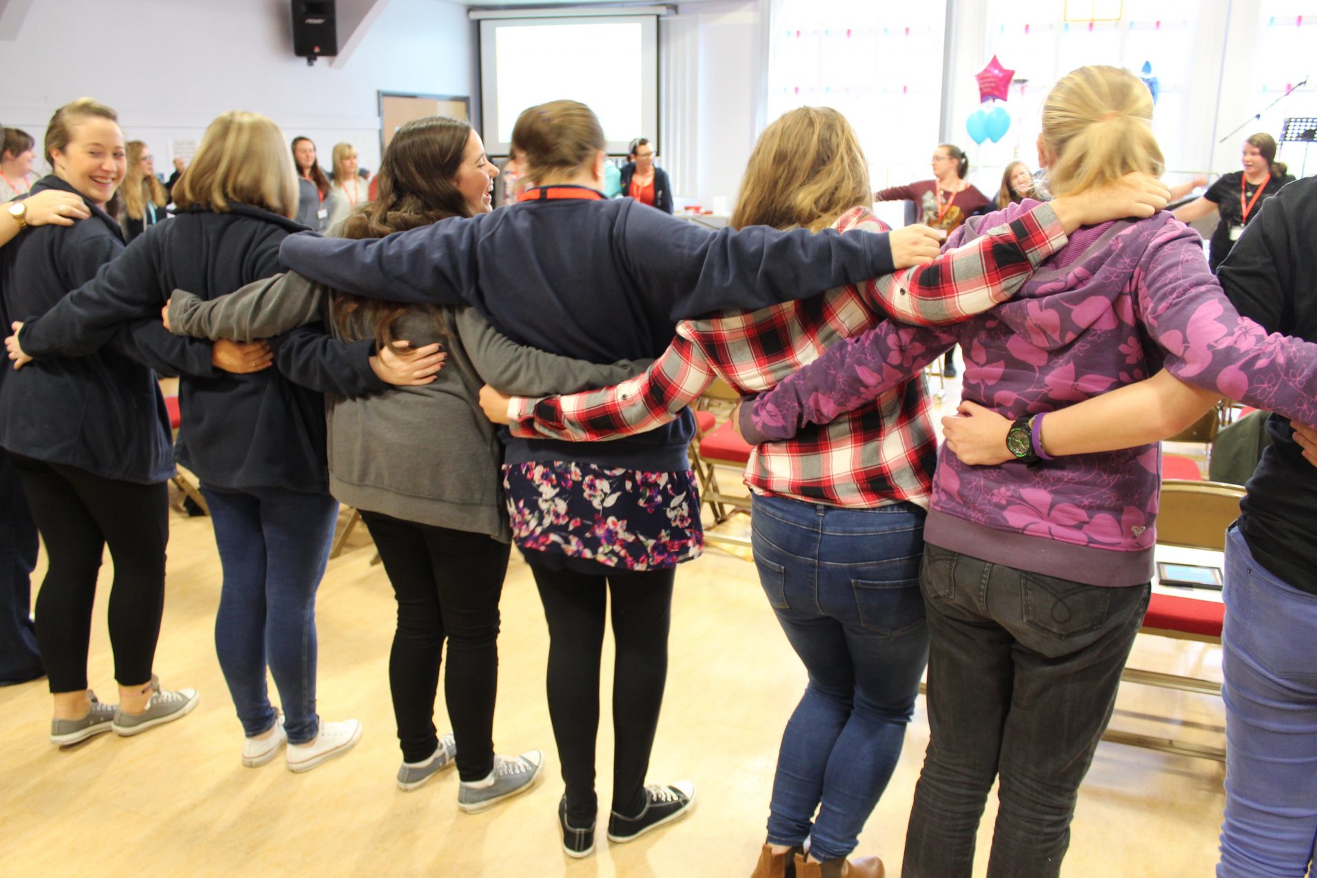 young women stood in a circle with arms around each other