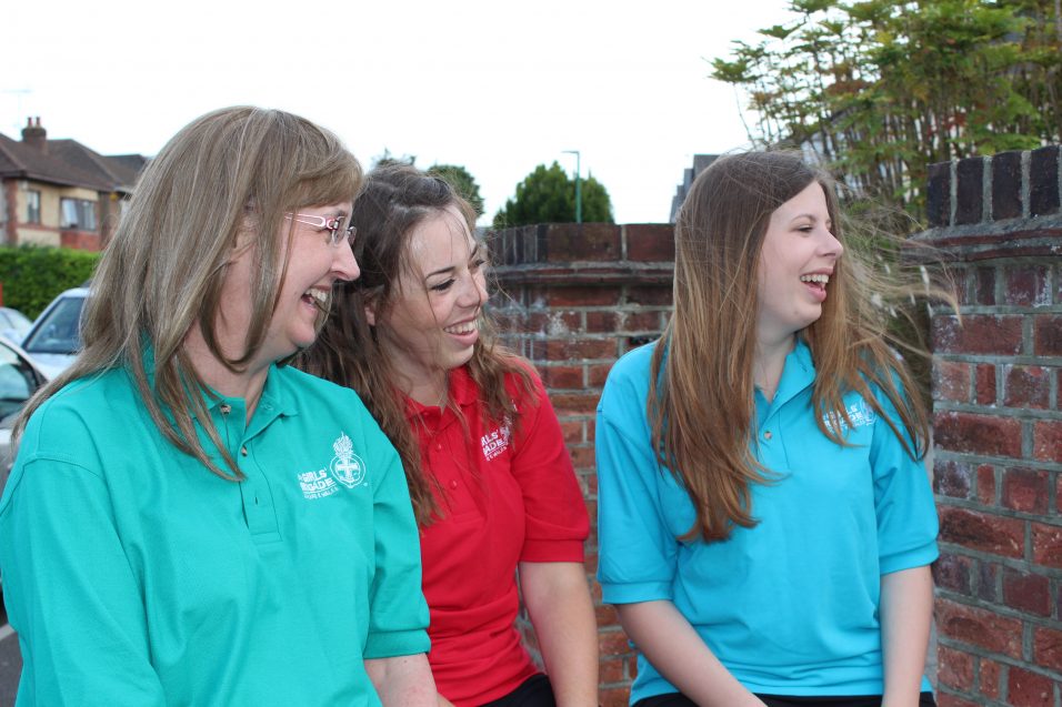 three Girls' Brigade volunteers sat on wall laughing