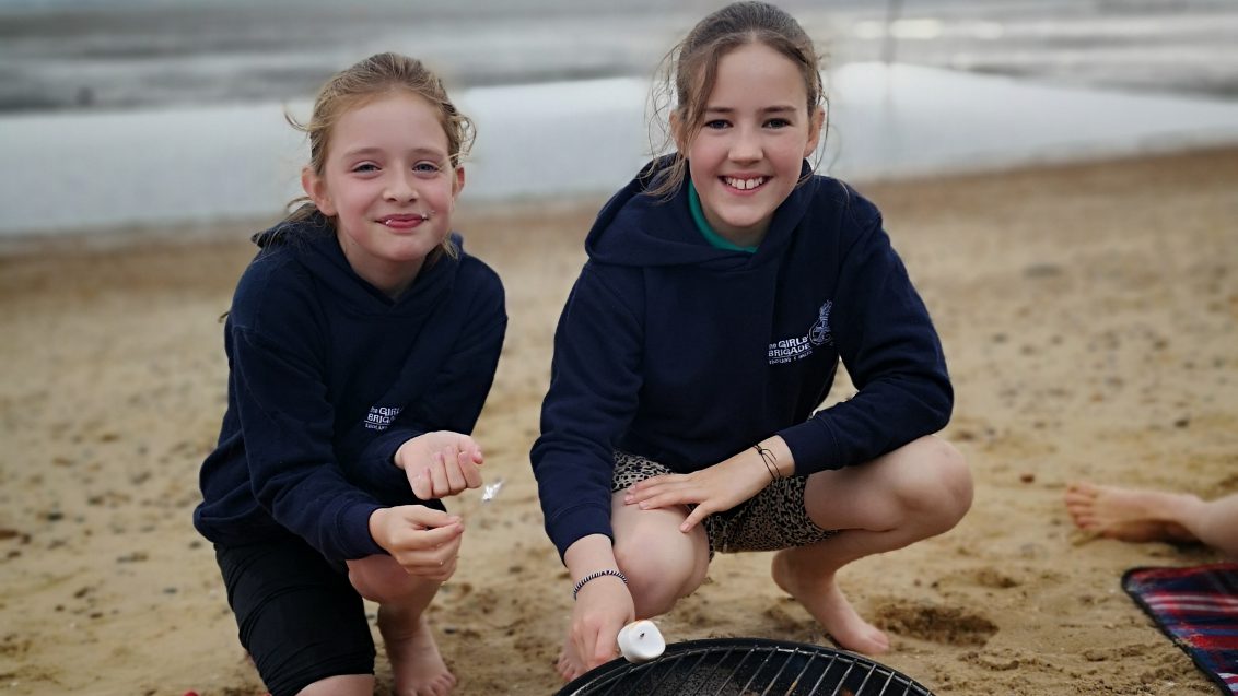 two girls toasting marshmallows on beach