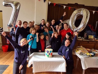 GB members and volunteers gathered around a cake with a '70' balloon