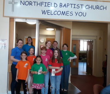 GB members wearing coffee shop t-shirts under church welcome sign